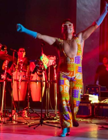 Erik Castrejón se encuentra sobre el escenario del Auditorio del Parque Papagayo de Acapulco con los brazos levantados y un micrófono en una de sus manos, mientras los músicos de su banda permanecen detrás de él durante el concierto homenaje a Juan Gabriel Amor eterno, rolitas de Juanga para mamá.
