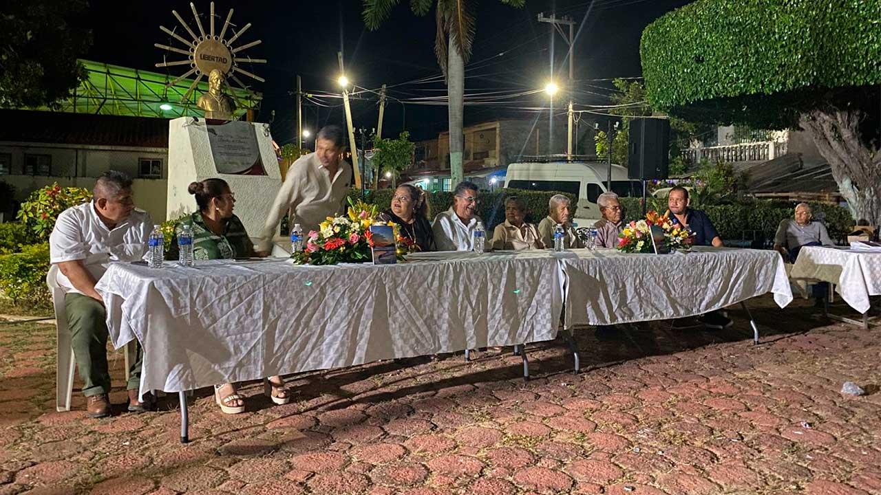 El escritor Luis Marín Sánchez sentado en la mesa de honor junto a autoridades y participantes del evento cultural, durante la presentación de su libro Noches serenas con sabor a mar en San Nicolás, Coyuca de Benítez.