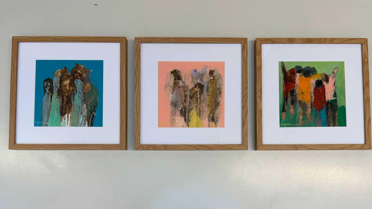 Tres obras pictóricas del artista guerrerense Héctor Massiel montadas en una pared blanca durante la exposición «Le Mexique en Couleurs» en el Teatro del Altigone, Francia. Las pinturas muestran figuras estilizadas y colores vibrantes sobre bastidores que conservan texturas orgánicas.
