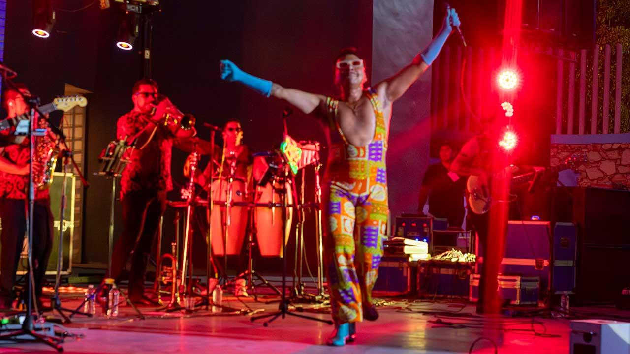 Erik Castrejón se encuentra sobre el escenario del Auditorio del Parque Papagayo de Acapulco con los brazos levantados y un micrófono en una de sus manos, mientras los músicos de su banda permanecen detrás de él durante el concierto homenaje a Juan Gabriel Amor eterno, rolitas de Juanga para mamá.