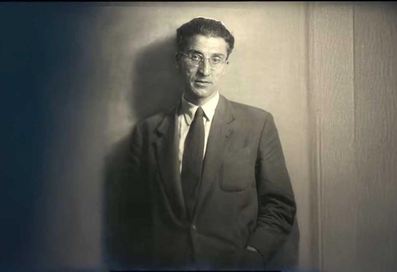 Fotografía en blanco y negro de Cesare Pavese, poeta y escritor italiano, vestido con traje formal y gafas, posando frente a una pared neutra. Imagen icónica que refleja su mirada introspectiva y su profunda conexión con la literatura del siglo XX.
