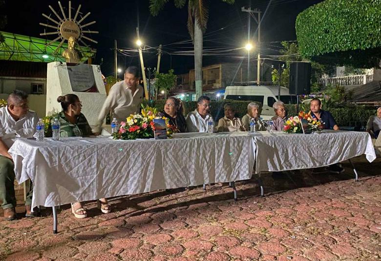 El escritor Luis Marín Sánchez sentado en la mesa de honor junto a autoridades y participantes del evento cultural, durante la presentación de su libro Noches serenas con sabor a mar en San Nicolás, Coyuca de Benítez.