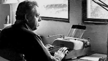 Jorge Ibargüengoitia sentado frente a su máquina de escribir, trabajando con concentración