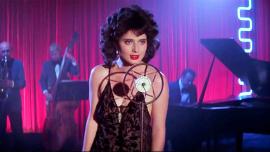 Isabella Rossellini, con un vestido azul y una expresión melancólica, canta en un escenario con iluminación tenue en una escena icónica de Blue Velvet de David Lynch.