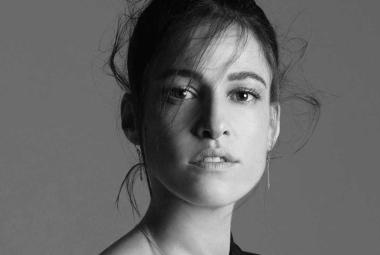 Retrato en blanco y negro del rostro de la fadista portuguesa Carminho. Expresión serena y mirada directa, con iluminación suave que resalta sus rasgos y transmite intensidad emocional. La imagen evoca la profundidad del fado y la conexión auténtica de la artista con su tradición