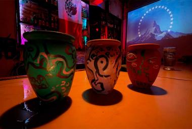 Tres cantaritos de barro pintados a mano sobre la barra del Bar del Puerto, iluminados con luces de colores y con una proyección al fondo.