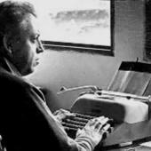 Jorge Ibargüengoitia sentado frente a su máquina de escribir, trabajando con concentración