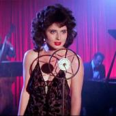 Isabella Rossellini, con un vestido azul y una expresión melancólica, canta en un escenario con iluminación tenue en una escena icónica de Blue Velvet de David Lynch.