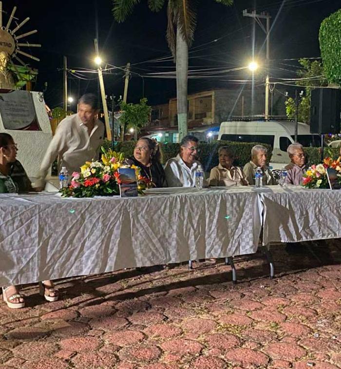 El escritor Luis Marín Sánchez sentado en la mesa de honor junto a autoridades y participantes del evento cultural, durante la presentación de su libro Noches serenas con sabor a mar en San Nicolás, Coyuca de Benítez.